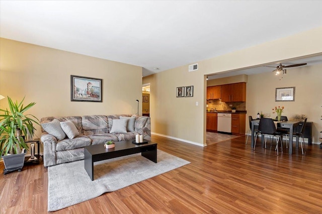 living room featuring a ceiling fan, baseboards, visible vents, and light wood finished floors