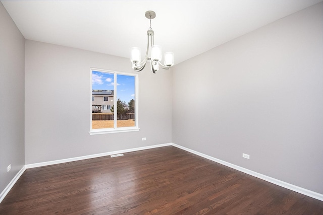 spare room with an inviting chandelier, dark wood-style floors, baseboards, and visible vents