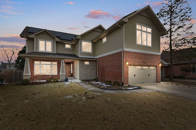 view of front of home with brick siding, roof mounted solar panels, an attached garage, and driveway