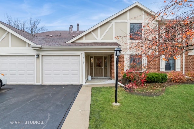 tudor-style house with brick siding, driveway, a front lawn, and a garage