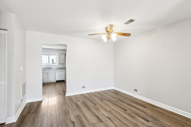 empty room with visible vents, a ceiling fan, and wood finished floors