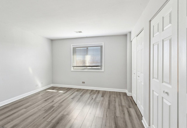 unfurnished bedroom with visible vents, wood finished floors, and baseboards