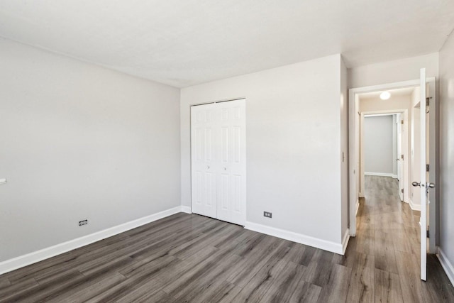 unfurnished bedroom featuring a closet, baseboards, and dark wood-style floors