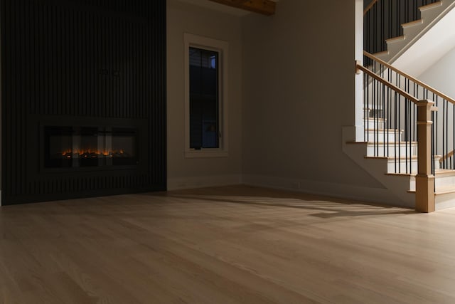 unfurnished living room with stairs, a glass covered fireplace, and wood finished floors