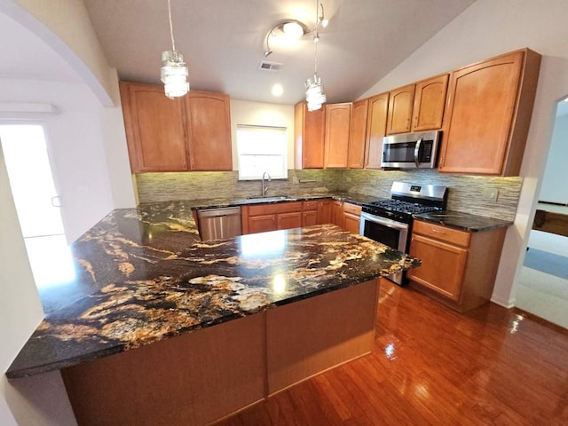 kitchen featuring lofted ceiling, dark stone countertops, arched walkways, stainless steel appliances, and a sink