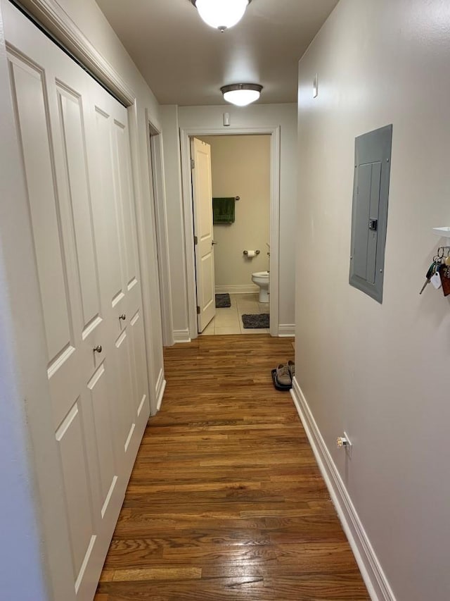 corridor featuring electric panel, baseboards, and wood finished floors