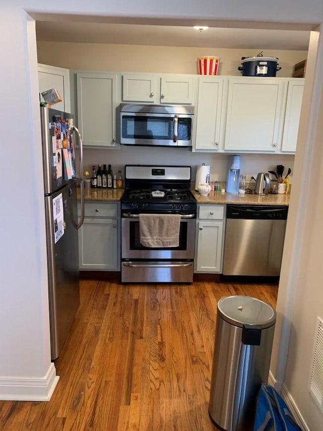 kitchen with visible vents, wood finished floors, white cabinetry, appliances with stainless steel finishes, and baseboards