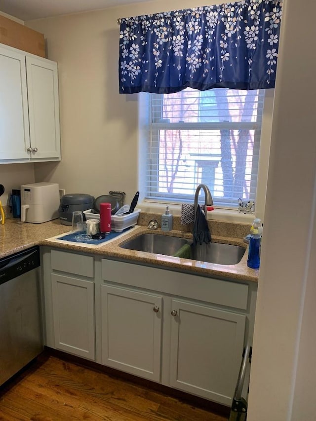 kitchen with dark wood finished floors, light countertops, stainless steel dishwasher, white cabinets, and a sink