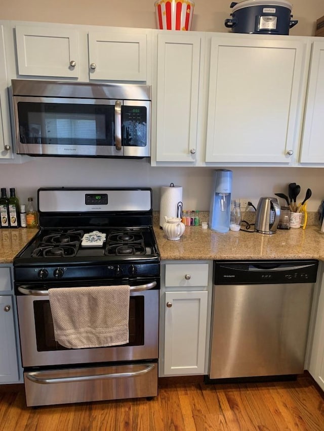 kitchen featuring white cabinets, wood finished floors, light stone countertops, and stainless steel appliances