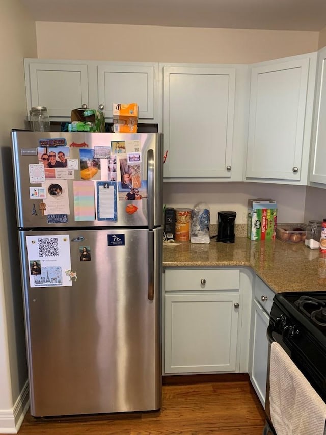 kitchen featuring stone countertops, wood finished floors, white cabinetry, gas stove, and freestanding refrigerator