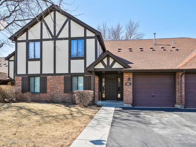 tudor home featuring brick siding, an attached garage, and a shingled roof