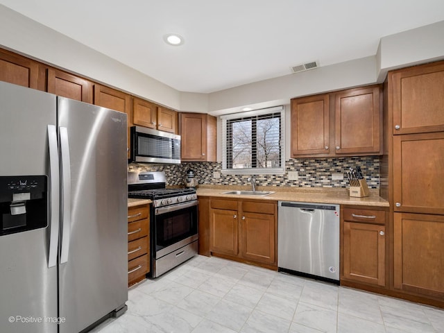 kitchen with visible vents, light countertops, appliances with stainless steel finishes, brown cabinetry, and a sink