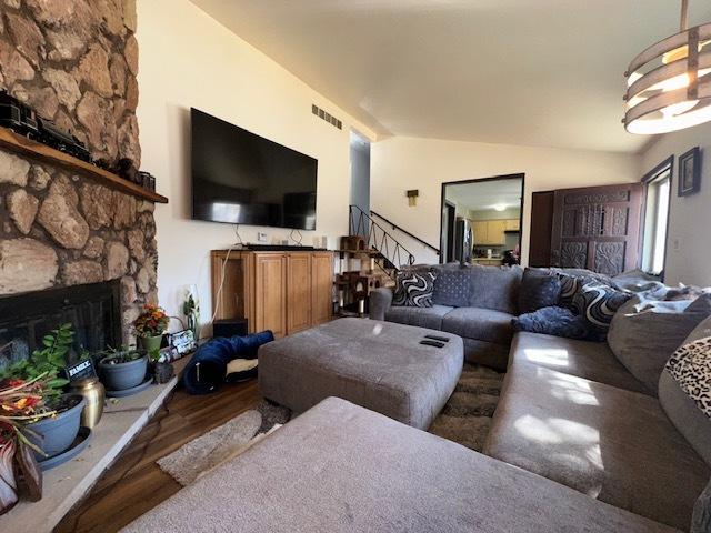 living room featuring stairway, wood finished floors, visible vents, a stone fireplace, and vaulted ceiling