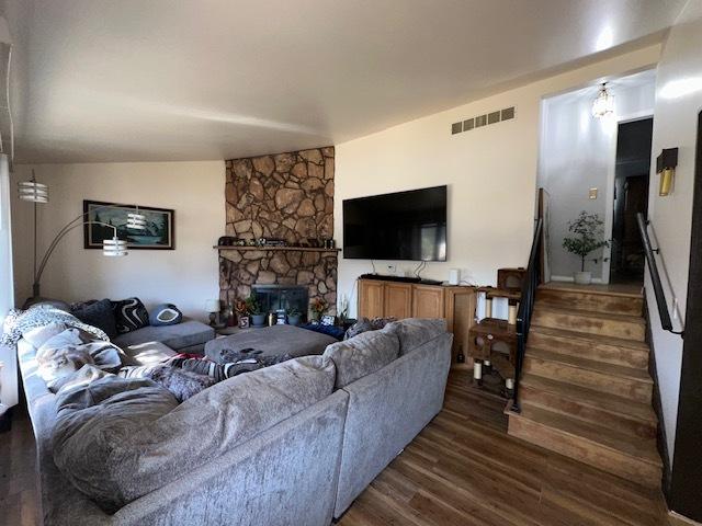 living room with visible vents, stairway, lofted ceiling, a stone fireplace, and dark wood-style floors