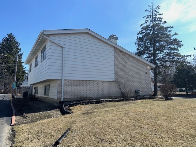 view of side of home featuring brick siding, a lawn, a chimney, and central AC