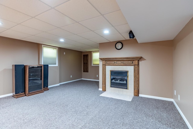 unfurnished living room featuring baseboards, a drop ceiling, a tile fireplace, wine cooler, and carpet flooring