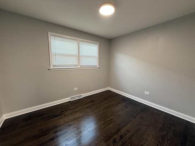 unfurnished room featuring dark wood-style floors, visible vents, and baseboards