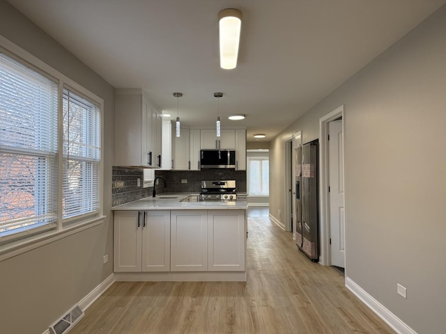 kitchen featuring tasteful backsplash, light countertops, light wood-style flooring, a peninsula, and stainless steel appliances