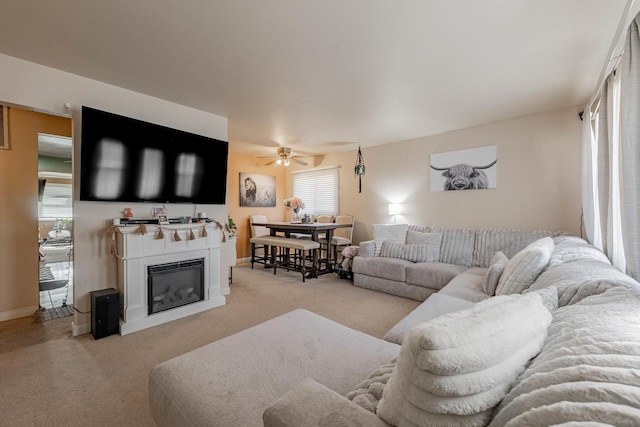 living area with a glass covered fireplace, carpet flooring, a ceiling fan, and baseboards