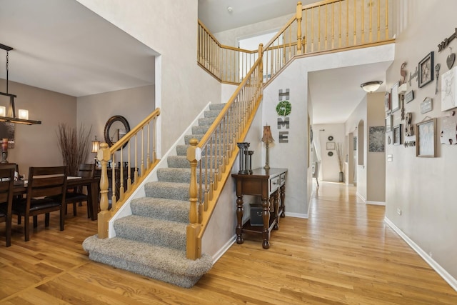 stairway with wood finished floors, baseboards, a towering ceiling, and a chandelier