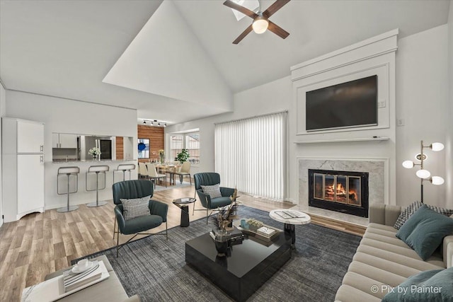 living area with high vaulted ceiling, a fireplace, wood finished floors, and a ceiling fan