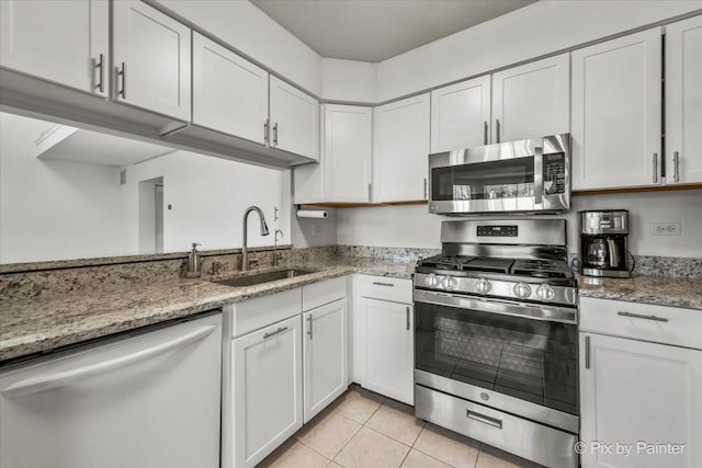 kitchen featuring light stone countertops, light tile patterned floors, appliances with stainless steel finishes, white cabinetry, and a sink