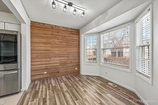 unfurnished dining area with light wood finished floors, wooden walls, track lighting, visible vents, and baseboards