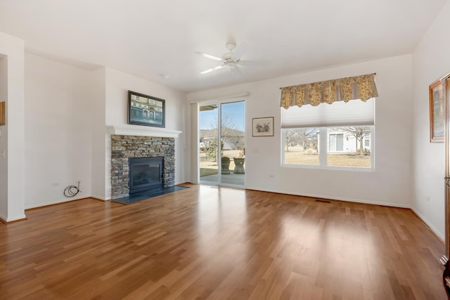 unfurnished living room featuring visible vents, a ceiling fan, wood finished floors, a stone fireplace, and baseboards