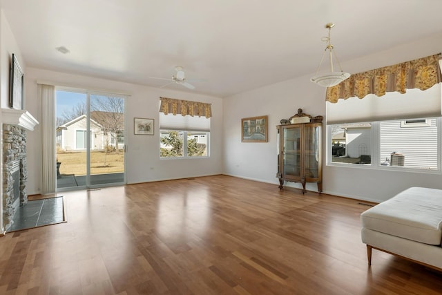 living area with baseboards, wood finished floors, a stone fireplace, and ceiling fan