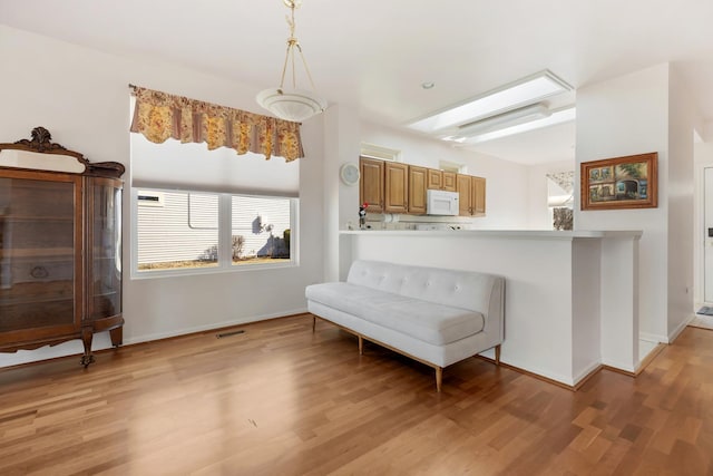 sitting room featuring visible vents, a skylight, light wood-type flooring, and baseboards