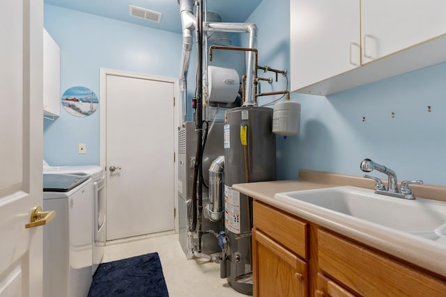 clothes washing area featuring visible vents, cabinet space, water heater, a sink, and washing machine and dryer