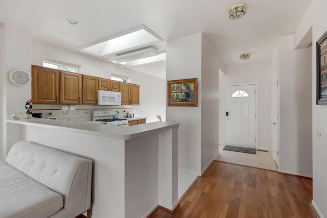 kitchen with light countertops, light wood-style flooring, a peninsula, brown cabinetry, and white appliances