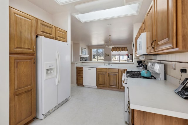 kitchen with brown cabinets, a sink, white appliances, light countertops, and light floors