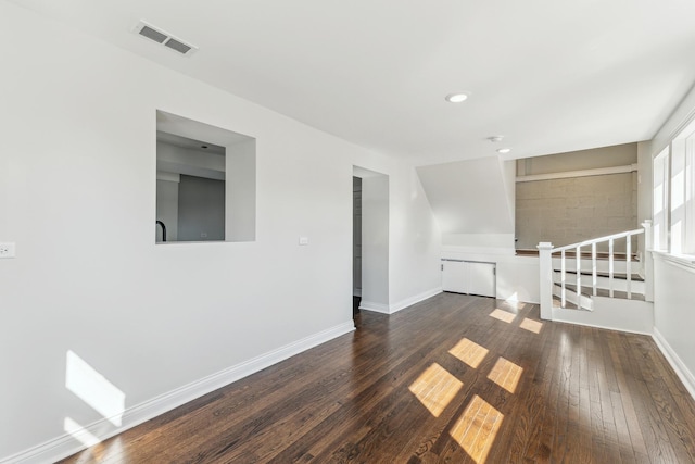 empty room with dark wood finished floors, visible vents, and baseboards