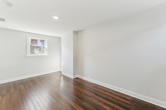 unfurnished room featuring dark wood-type flooring, visible vents, and baseboards