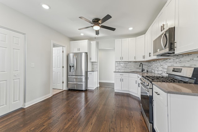 kitchen with dark wood finished floors, stone counters, stainless steel appliances, a ceiling fan, and a sink