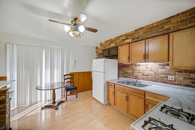 kitchen featuring a wainscoted wall, a ceiling fan, a sink, white appliances, and light countertops