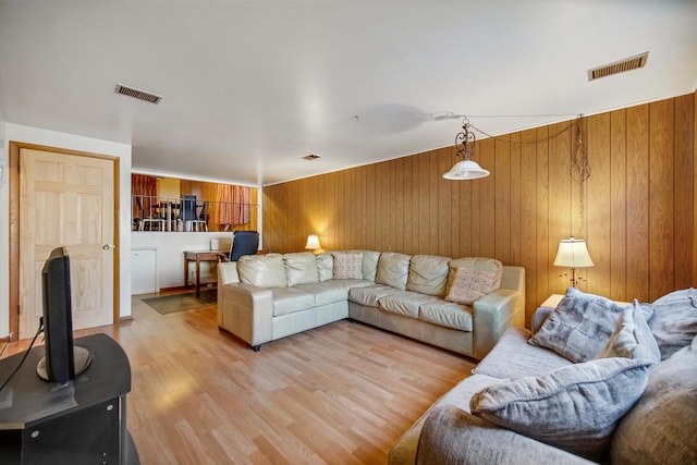 living room featuring light wood finished floors, visible vents, and wooden walls