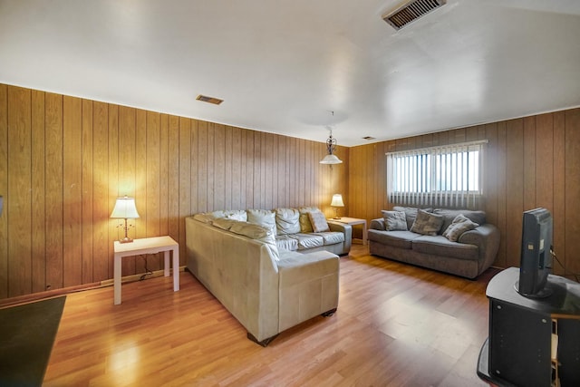 living area with light wood-type flooring, visible vents, and wood walls