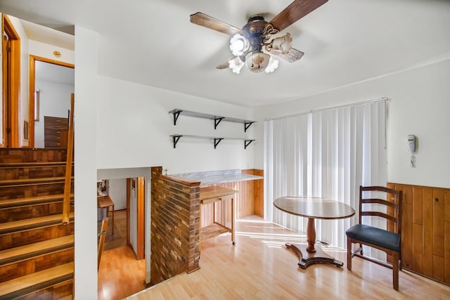 sitting room featuring wood finished floors, stairway, wood walls, wainscoting, and ceiling fan