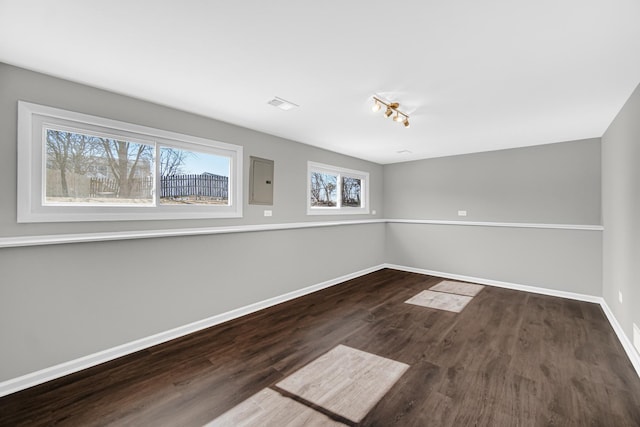 spare room featuring electric panel, visible vents, baseboards, and wood finished floors