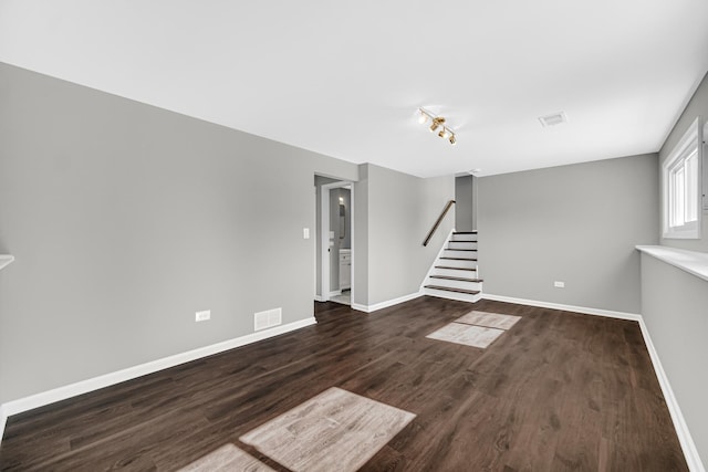 unfurnished living room with dark wood finished floors, visible vents, stairway, and baseboards