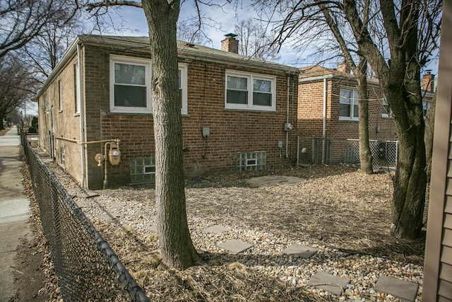 back of property with brick siding, a chimney, and fence