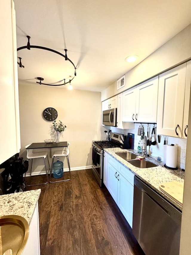 kitchen with a sink, light stone counters, dark wood finished floors, appliances with stainless steel finishes, and white cabinets