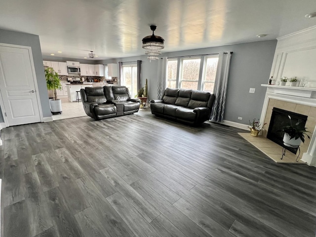 unfurnished living room with a notable chandelier, wood finished floors, baseboards, and a tile fireplace