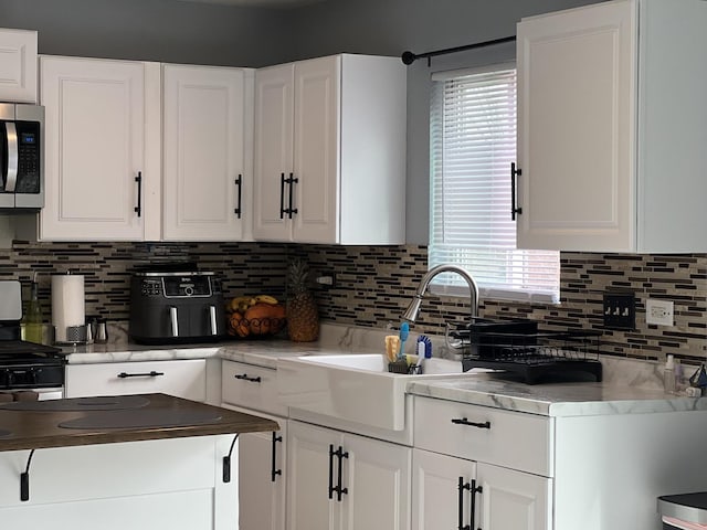 kitchen featuring stainless steel microwave, white cabinets, tasteful backsplash, and a sink