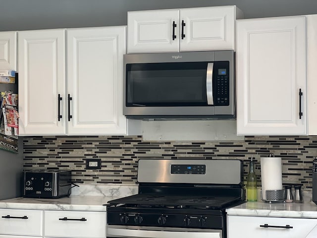 kitchen with light stone counters, decorative backsplash, white cabinetry, and stainless steel appliances