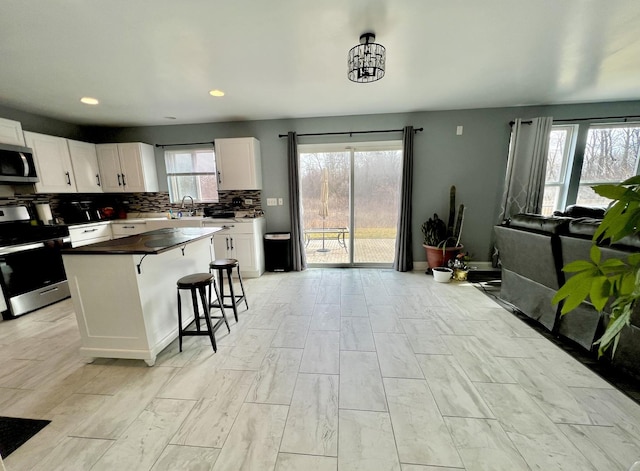 kitchen featuring a sink, stainless steel appliances, white cabinetry, tasteful backsplash, and a center island