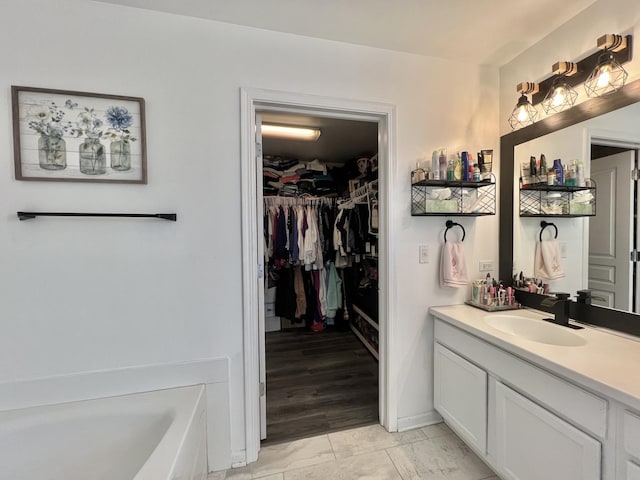 bathroom featuring a garden tub, a spacious closet, and vanity