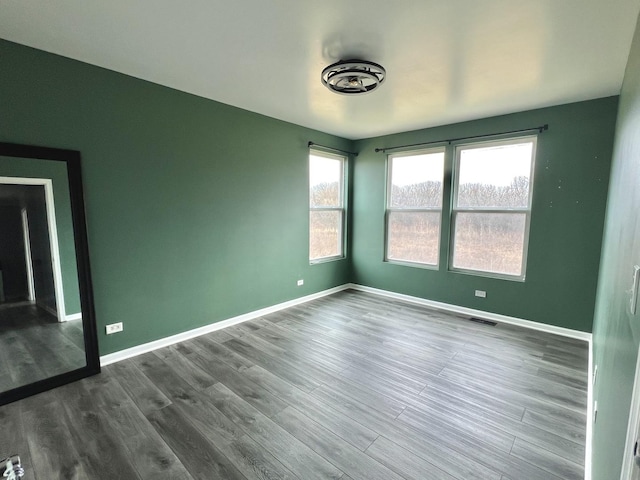 empty room with visible vents, dark wood-type flooring, and baseboards